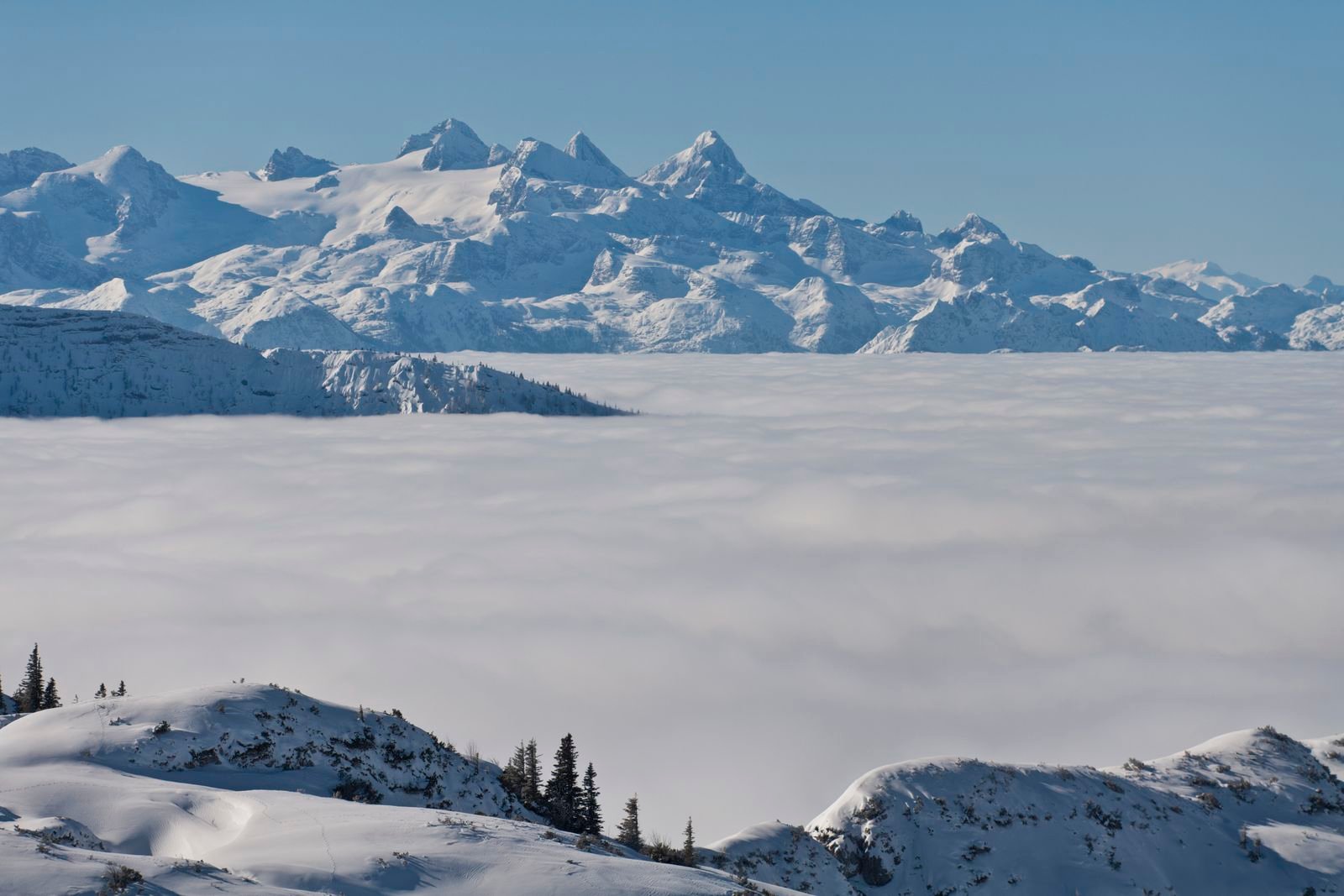 Snow-covered Feuerkogel plateau and distant mountains above the cloud layer